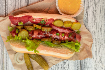 One Hot Dog with mustard, pickled cucumber, onion and lettuce leaves on a light background. Fast food, street meal. Top view