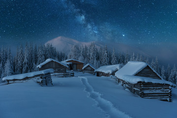 Fairytale landscapes of the winter Carpathian Mountains with a charming milky way in the sky tourist tents and snowy houses in the valleys