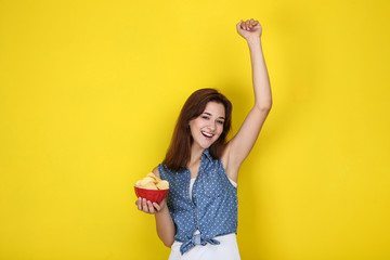 Young woman with potato chips in bowl on yellow background