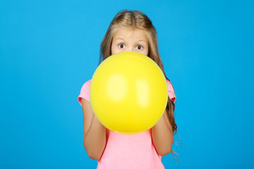 Fototapeta na wymiar Pretty little girl blowing yellow balloon on blue background