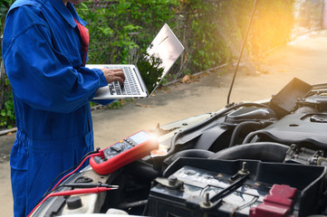 The auto repair technician is investigating and analyzing car problems using a notebook computer system to find the cause of the problem in order to check the customer's condition.