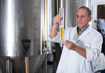 Adult expert is standing with flask for beer and analizying it