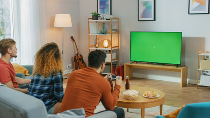 In the Living Room Three Friends Play Video Games on Green Chroma Key Screen, Using Controllers. Teenagers Having Fun at Home. © Gorodenkoff