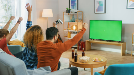 In the Living Room Three Friends Play Video Games on Green Chroma Key Screen, Using Controllers and Celebrates Win Doing YES Gesture and Raising Arms Up. Teenagers Having Fun at Home. © Gorodenkoff