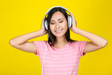 Beautiful woman with headphones on yellow background