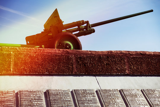 Memorial complex in honor of the memory of those killed in world war II. A plaque with the names of the dead soldiers and the Soviet anti-tank gun ZIS-2 against the sky.