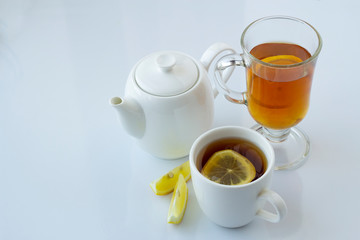 Tea with lemon in a white and glass cup and a white teapot on a white background