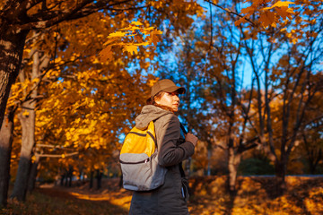 Naklejka na ściany i meble Tourist with backpack walking in autumn forest. Young woman travel at sunset