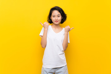 Asian young woman over isolated yellow wall with thumbs up gesture and smiling