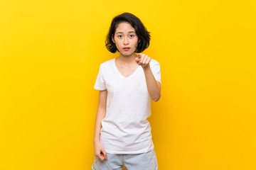 Asian young woman over isolated yellow wall surprised and pointing front