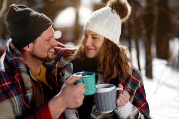 Couple in love enjoying a tender moment in fresh snow during wintertime and drinking hot chocolate...