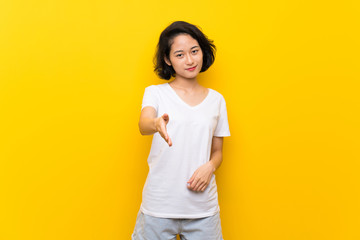 Asian young woman over isolated yellow wall shaking hands for closing a good deal