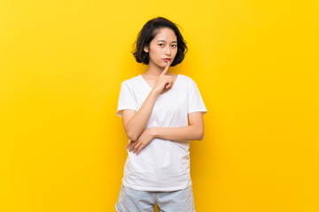 Asian young woman over isolated yellow wall showing a sign of silence gesture putting finger in...