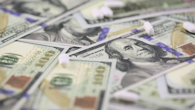 Prescription pills falling onto a background on one hundred dollar bills cash