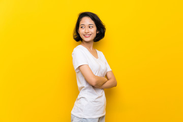 Obraz premium Asian young woman over isolated yellow wall with arms crossed and happy