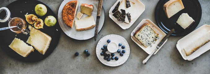 Wine snack variety. Flat-lay of cheeses, apricot jam, fresh fruit and crackers over rough grey...
