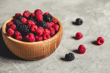 raspberries and blackberries in wood bowl on gray table, vintage