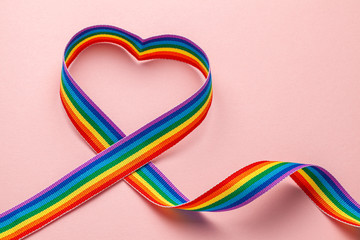 LGBT rainbow ribbon in the shape of heart. Pride tape symbol. Pink background