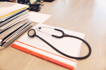 Stethoscope with black medical clipboard on wooden desk