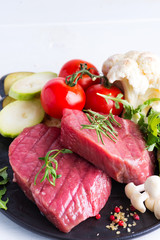 Raw beef steak with fresh vegetables in a pan on a marble background, top view