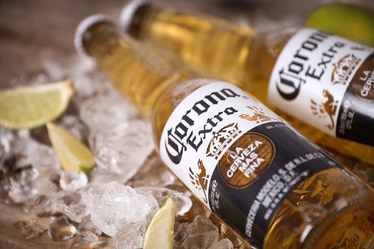 Two corona extra lager beer bottles  on ice with lime slices on a rustic wooden table - Cerveceria Modelo in Mexico