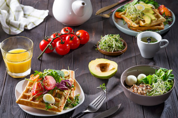 Belgian Waffles with avocado, eggs, micro green and tomatoes with orange juice and tea on wooden table. Perfect breakfast for healthy food or lose weight. Avocado sandwich.