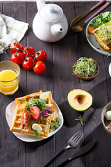 Belgian Waffles with avocado, eggs, micro green and tomatoes with orange juice and tea on wooden table. Perfect breakfast for healthy food or lose weight. Avocado sandwich.
