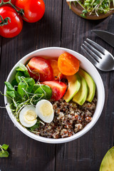Fresh healthy salad with quinoa, cherry tomatoes and mixed greens, avocado, egg and micro greens on wood background top view. Food and health. Superfood meal. Clean eating. Healthy lifestyle