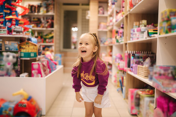 Adorable little girl shopping for toys. Cute female in toy store. Happy young girl selecting toy