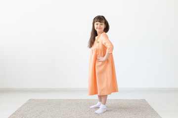 Beautiful little girl in a peach dress posing against a white wall. The concept of children's designer clothes.