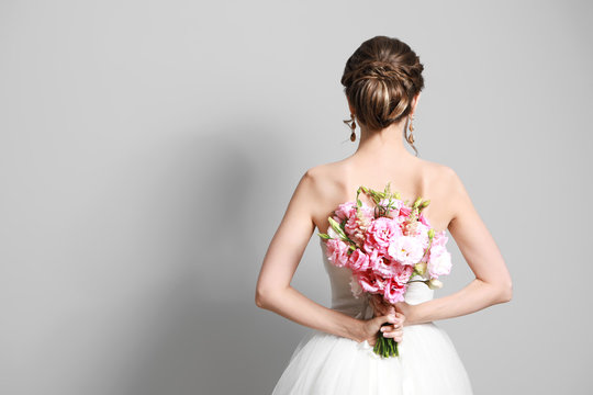 Beautiful young bride with wedding bouquet on grey background,  back view