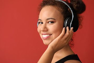 Beautiful African-American woman listening to music on color background