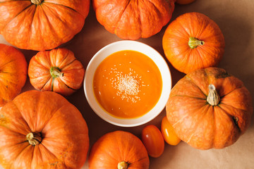 homemade fresh sweet pumpkin soup with sesame seeds in a plate on a table with pumpkins. Thanksgiving, vegetarian concept