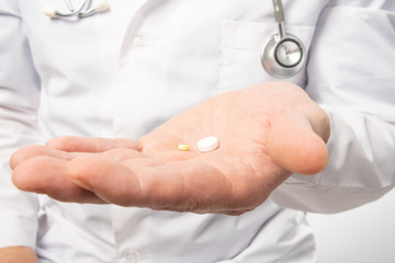 The doctor in white clothes, and blue gloves, with a stethoscope on his neck, holds out pills. Close up