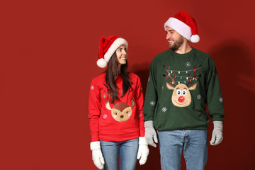 Young couple in Christmas sweaters and Santa hats on color background