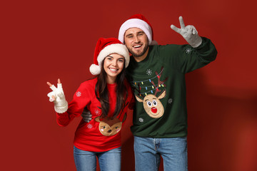 Fototapeta premium Young couple in Christmas sweaters and Santa hats on color background