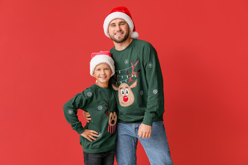 Happy man with his son in Christmas sweaters and Santa hats on color background