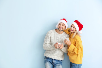Happy couple in Santa hats drinking hot chocolate on color background