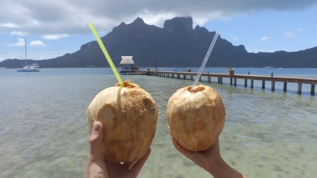 Travel icon fresh coconut water drinks at famous tourist destination Bora Bora, Tahiti, French Polynesia. Couple taking POV video having fun on adventure travel.