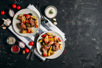 Meat with vegetables on a plate with garlic sauce and spices on a dark wooden background. Baked vegetables (zucchini, peppers, apples, tomatoes) and meat rolls with bacon. Top view. Place for text