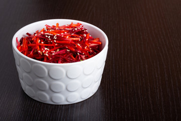 Vegetable salad of apple, carrot and beetroot with lemon juice, sesame seeds and vegetable oil in a white deep plate