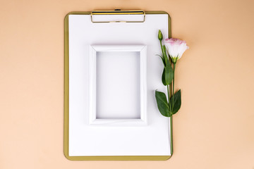 Clipboard with eustoma flower and white frame on beige paper background, flat lay. Post card mockup