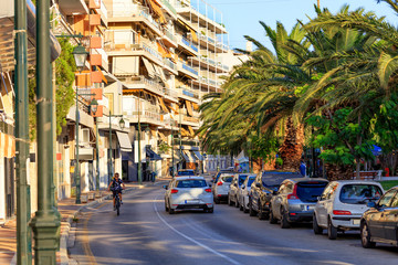 Street landscape of the summer city of Loutraki, Greece, with passing cars and a teenager on a bicycle.