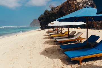 Wooden deck chairs with umbrellas along the coastline. Melasti Beach in the Indian Ocean. Indonesia, Bali.