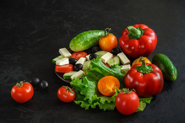 Set of fresh ripe whole and chopped vegetables for cooking Greek salad on a black concrete surface with space for text, advertisement or logo. shot from above at an angle