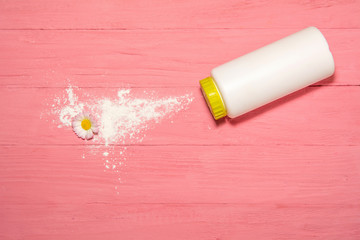 perfumed talcum powder for legs. white bottle with a salt cap top view. scattered talcum powder on a pink wooden board with pink flowers around the perimeter. white powder fragrance for the feet