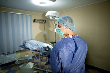 The surgeon stands with his back to the camera. Before him on the operating table lies a patient. Preparation for surgery