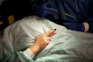 Surgeon and patient in operating room. Woman crossed her fingers for good luck before surgery. Surgeon holds scissors in his hand. Close up