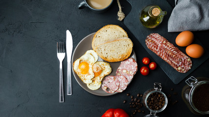 Jajka sadzone z chrupiącym chlebem, salami, pomidorami i kawą. Widok z góry.