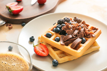 Plate with tasty waffles, chocolate and berries on table